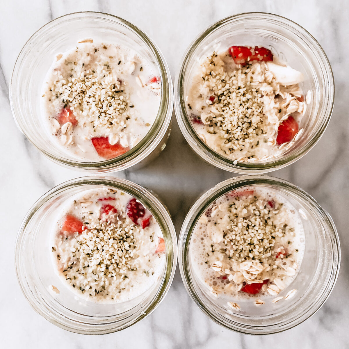 A look over 4 glass jars on a kitchen counter. They're filled with strawberry and cream overnight oats.